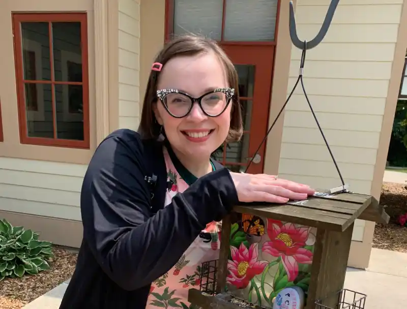 Danielle smiling beside a colorful handmade bird feeder