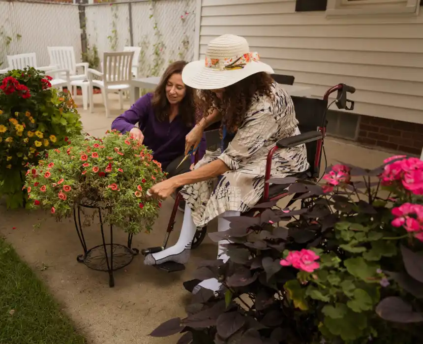 Woman in a wheelchair tending flowers with a caregiver